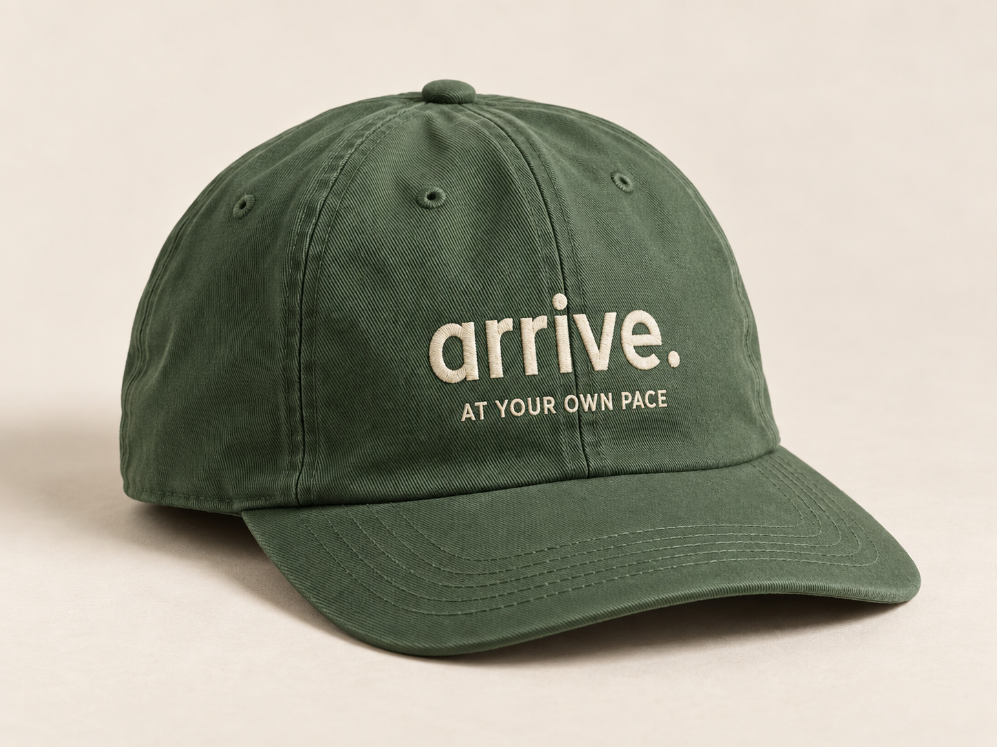 Generated photographic-style concept of an olive cotton cap with cream arrive lettering and visible embroidery texture.