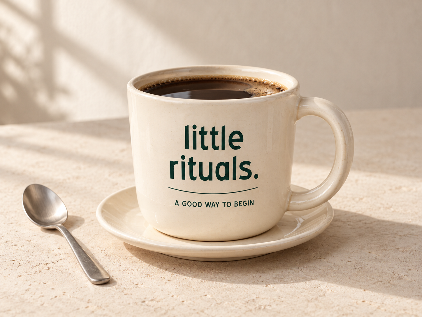 Generated photographic-style concept of a cream ceramic coffee cup with little rituals lettering, a matching saucer and a spoon.